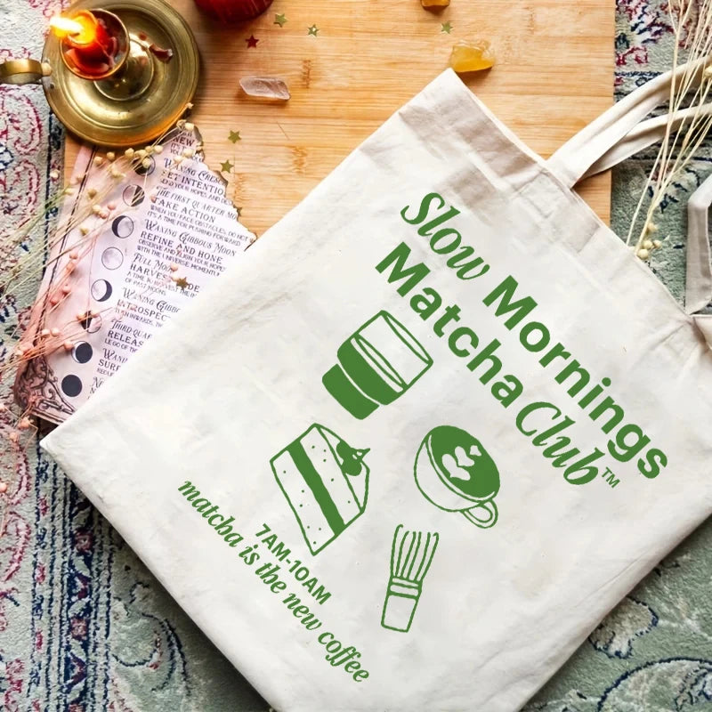 Sac shopping écologique avec typographie verte "Slow Mornings Matcha Club" et illustrations de gâteau et latte, célébrant la douceur du rituel matinal.