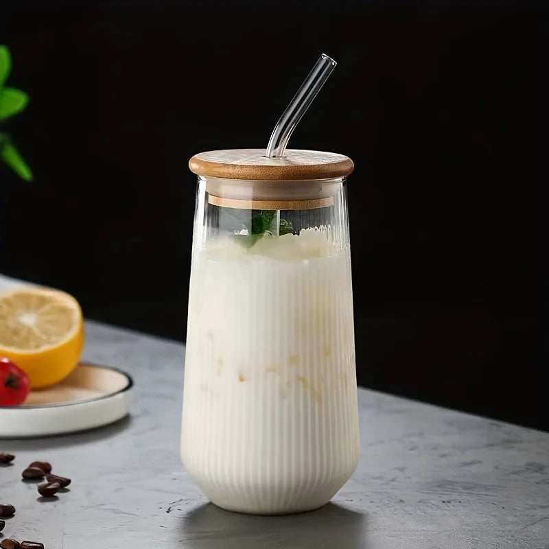 Mise en scène élégante sur fond sombre du verre Mistral contenant une boisson lactée glacée. Zoom sur la texture striée du verre borosilicate et le couvercle hermétique, parfait pour une utilisation café ou matcha.