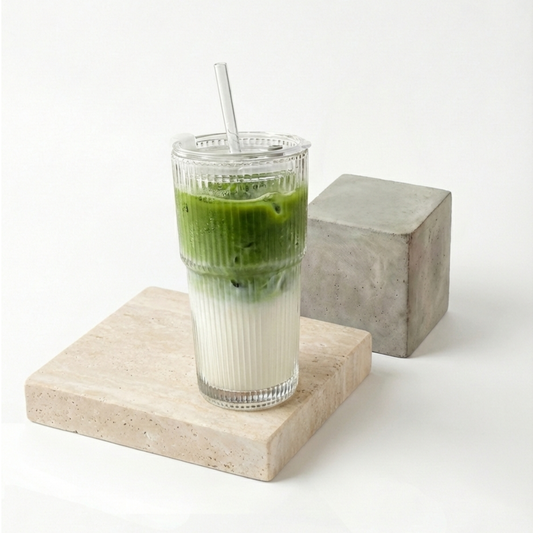 Gobelet en verre strié design (Lumina) rempli d'un Iced Matcha Latte bicolore, posé sur une pierre travertin avec son couvercle hermétique et sa paille en verre, illustrant le kit parfait pour l'été.