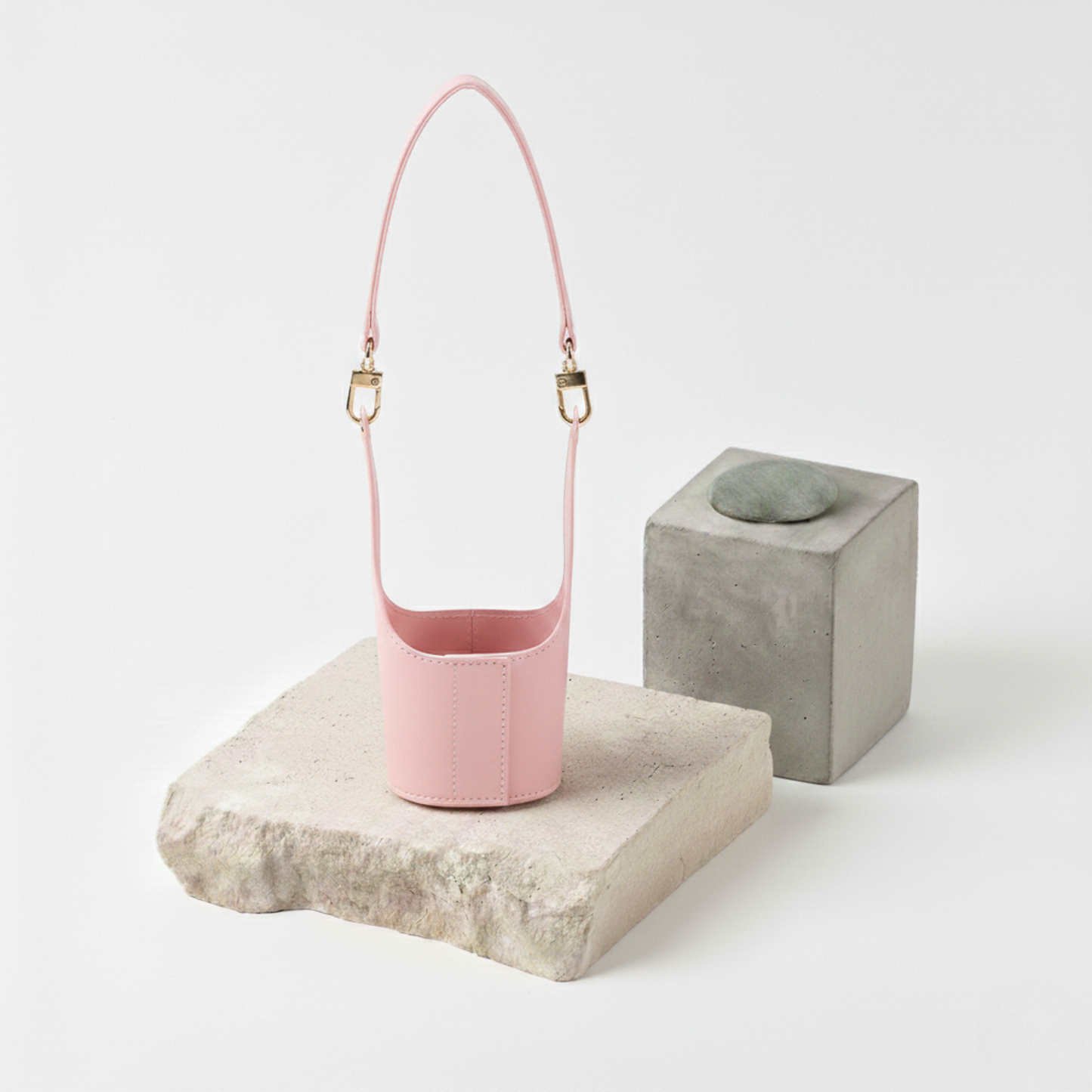 Étui porte-gobelet en cuir vegan lisse rose pastel avec une anse assortie et des boucles dorées, transformant votre boisson à emporter en un accessoire de mode féminin et élégant.