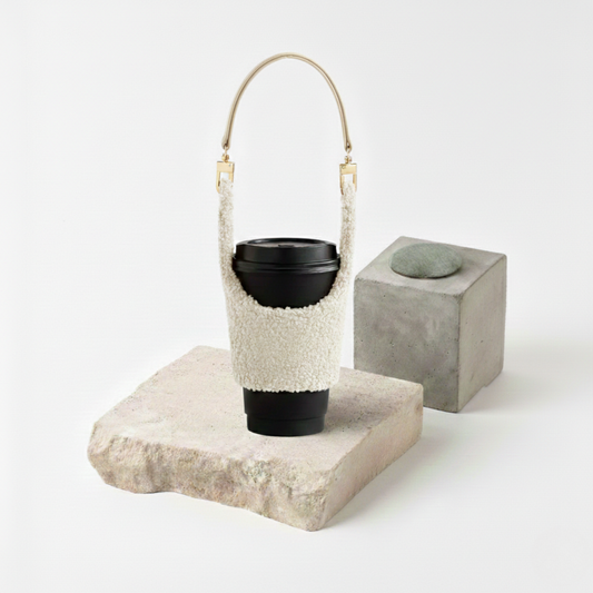 Manchon isolant pour gobelet en tissu pelucheux blanc crème (texture mouton/sherpa) avec une anse dorée élégante, transformant votre boisson en accessoire de mode hivernal.