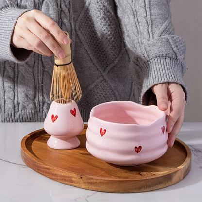 Mains préparant un thé matcha dans le bol Sakura rose, illustrant la taille généreuse du bol pour le fouettage et le design "Cœur" parfait pour offrir un moment de douceur.