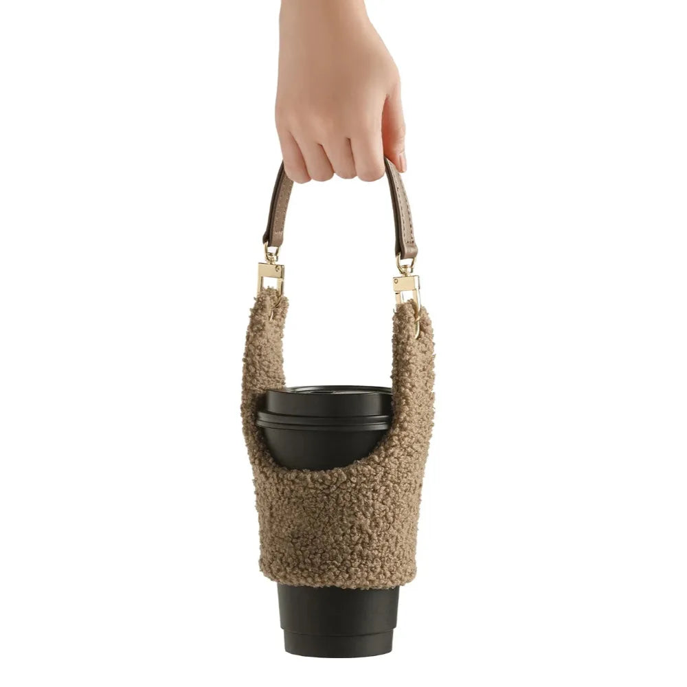 Main tenant le support de gobelet portable en peluche beige taupe foncé, parfait pour transporter votre Matcha Latte ou cappuccino lors de vos déplacements quotidiens avec style.