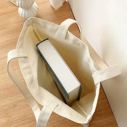 Vue en plongée de l'intérieur du sac en coton canvas épais contenant un gros livre, démontrant sa solidité et sa capacité idéale pour transporter livres, ordinateur ou affaires de cours.