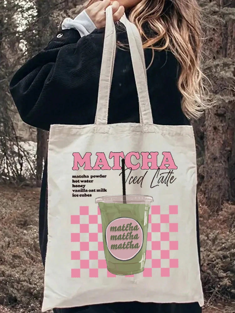Tote bag porté à l'épaule sur une tenue en jean, affichant un design esthétique rose à damier (checkerboard) avec l'inscription Matcha Iced Latte.