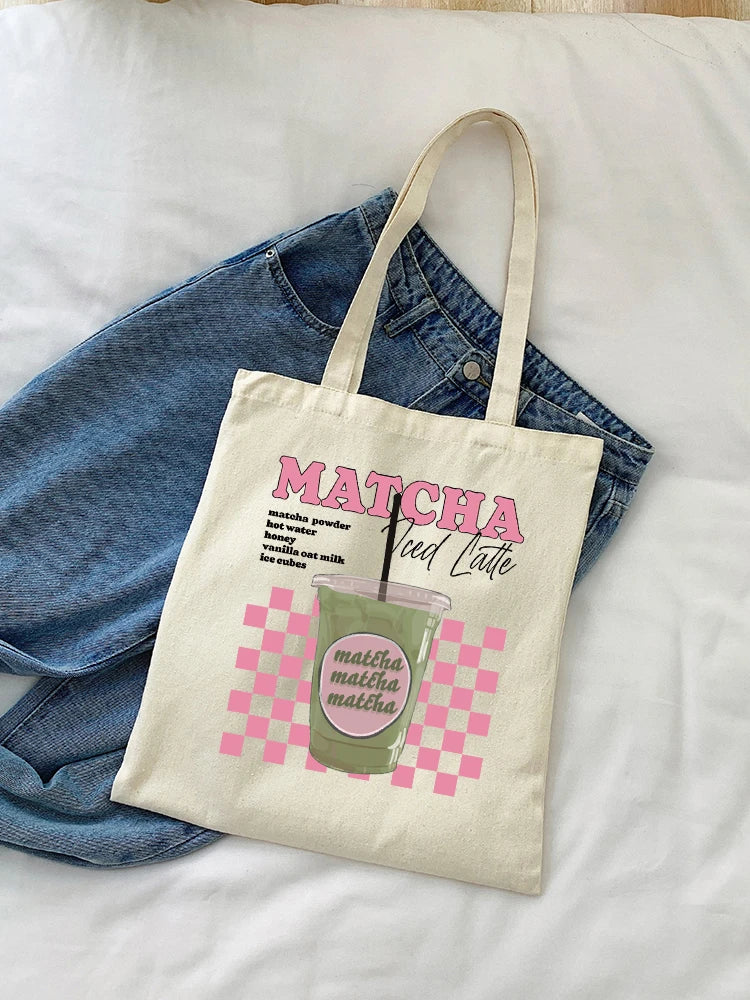 Tote bag posé sur un jean, affichant un design esthétique rose à damier (checkerboard) avec l'inscription Matcha Iced Latte.
